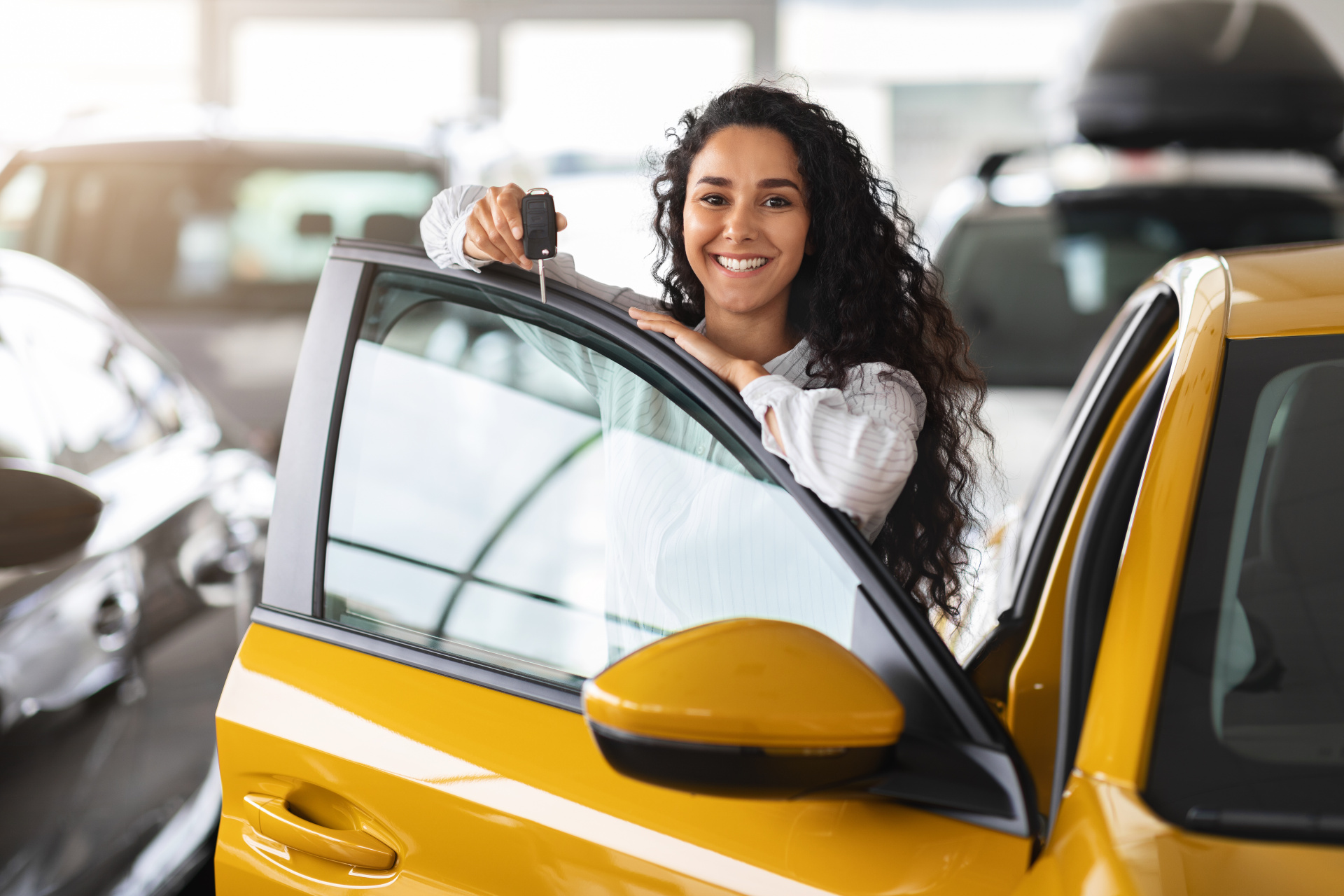 Cheerful brunette woman holding key, buying new car, showroom interior Cheerful brunette woman holding key, buying new car, showroom interior
