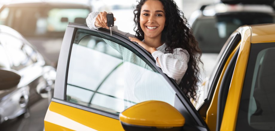Cheerful brunette woman holding key, buying new car, showroom interior Cheerful brunette woman holding key, buying new car, showroom interior