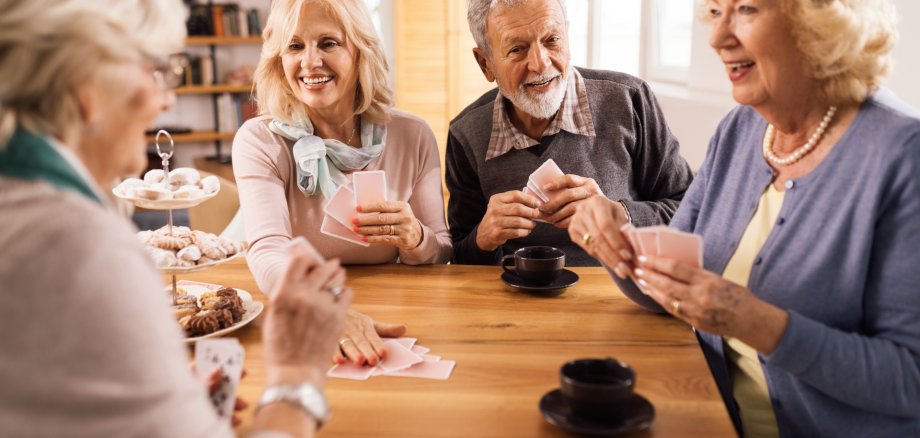 Happy mature couple playing card game with their friends at home.