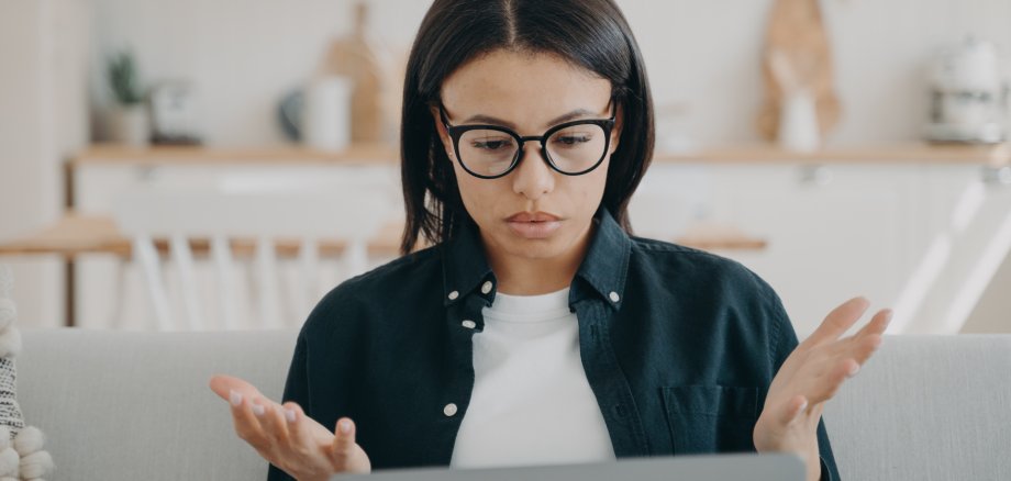 Puzzled woman freelancer in glasses spreading hands, shocked by problems in work, error on laptop