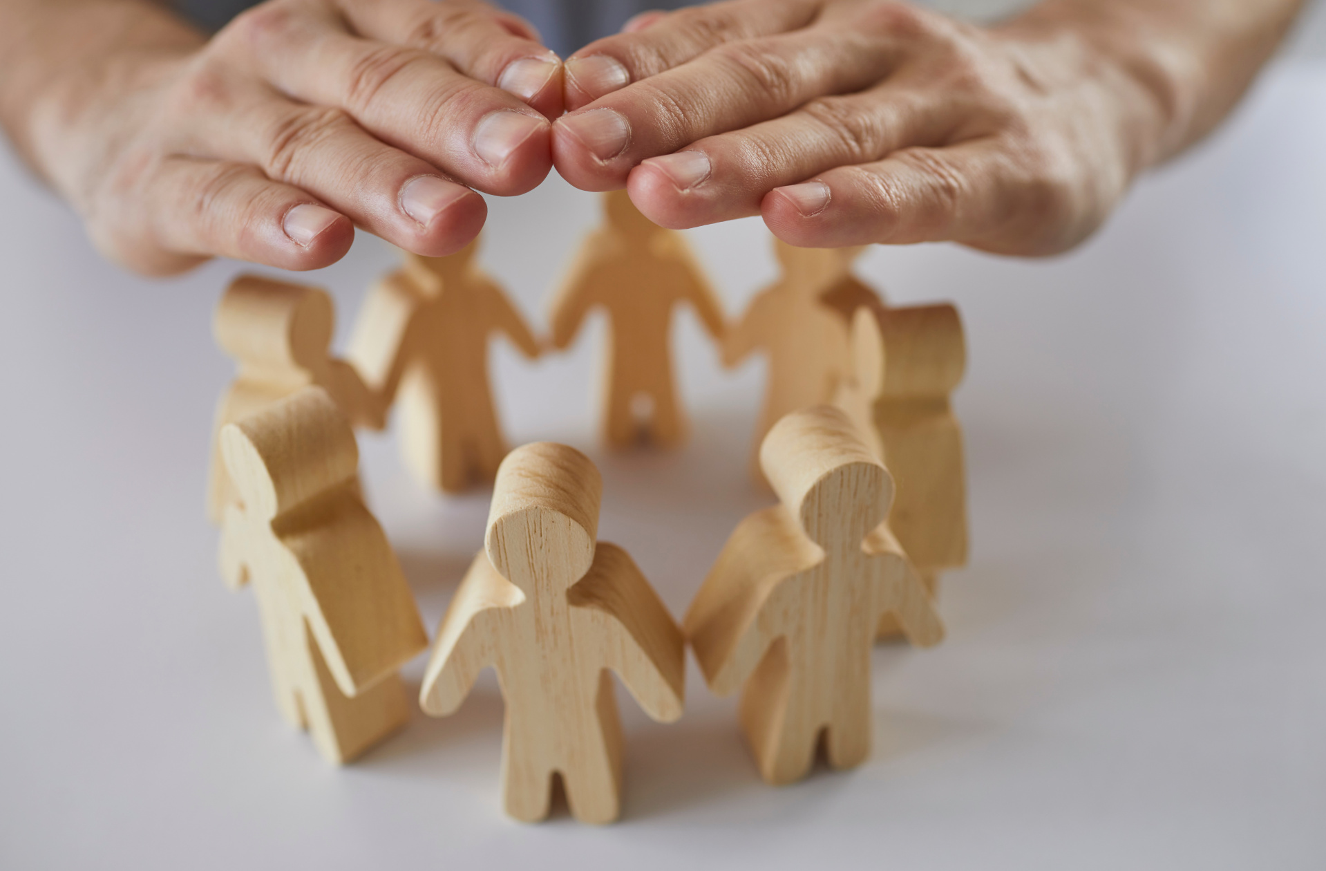 Insurance agent's hands protect wooden figures of people standing in circle in front of him. Insurance agent's hands protect wooden figures of people standing in circle in front of him.