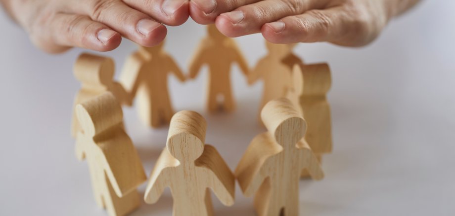 Insurance agent's hands protect wooden figures of people standing in circle in front of him. Insurance agent's hands protect wooden figures of people standing in circle in front of him.