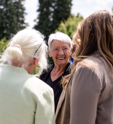 Eine Gruppe von Menschen unterschiedlichen Alters steht im Freien in einem Kreis und unterhält sich.