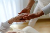Nahaufnahme von zwei Personen in weißer Kleidung. Eine Hand stützt und hält sanft die Hand eines älteren Menschen.