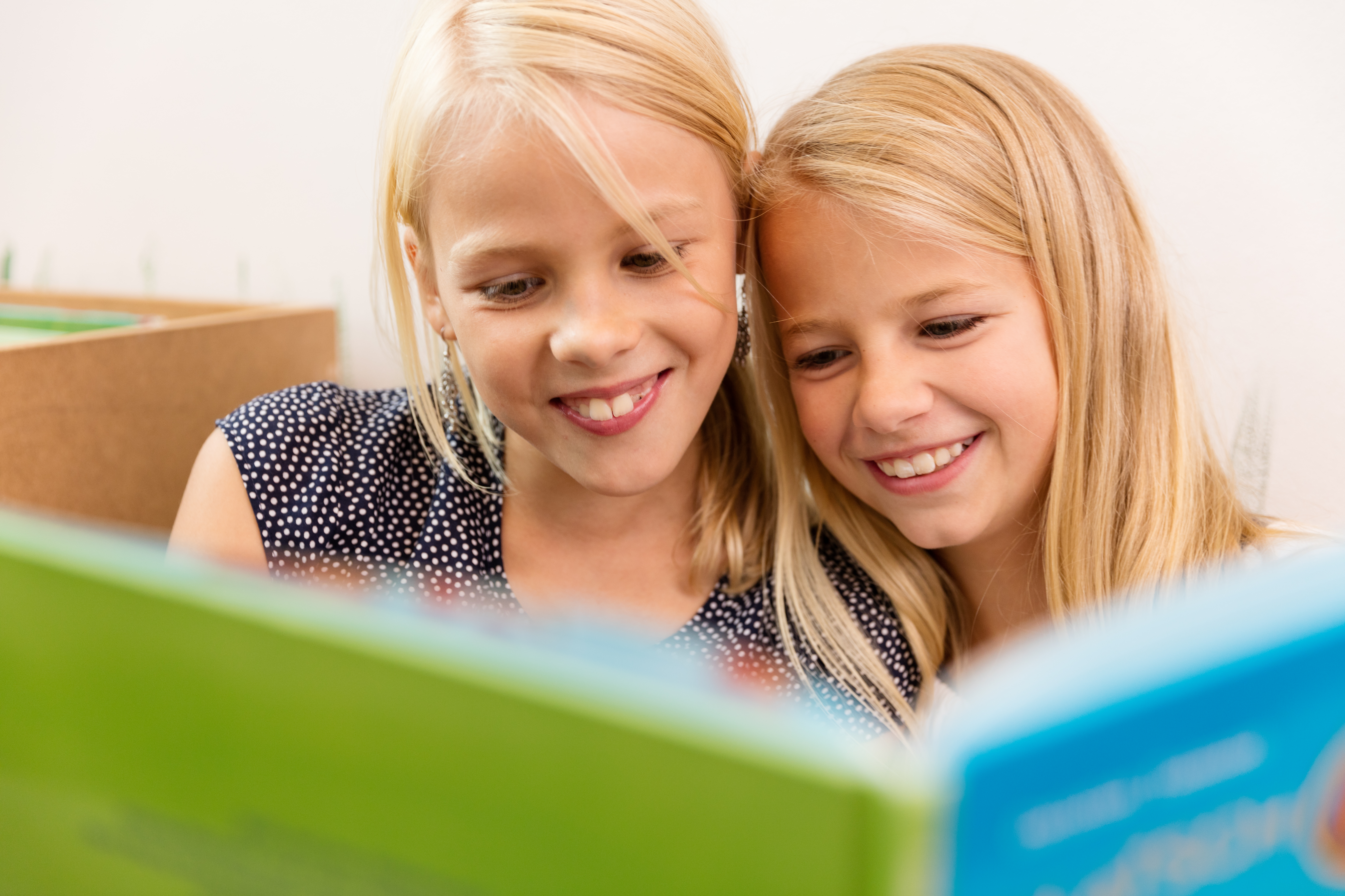 Zwei Mädchen lesen ein Buch Zwei Mädchen blicken lächelnd in ein farbiges Buch. Im Vordergrund sind die grünen und blauen Seiten des Buches zu sehen.