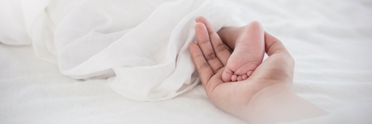 Nahaufnahme eines kleinen Babyfußes, der in der offenen Handfläche einer erwachsenen Person liegt.