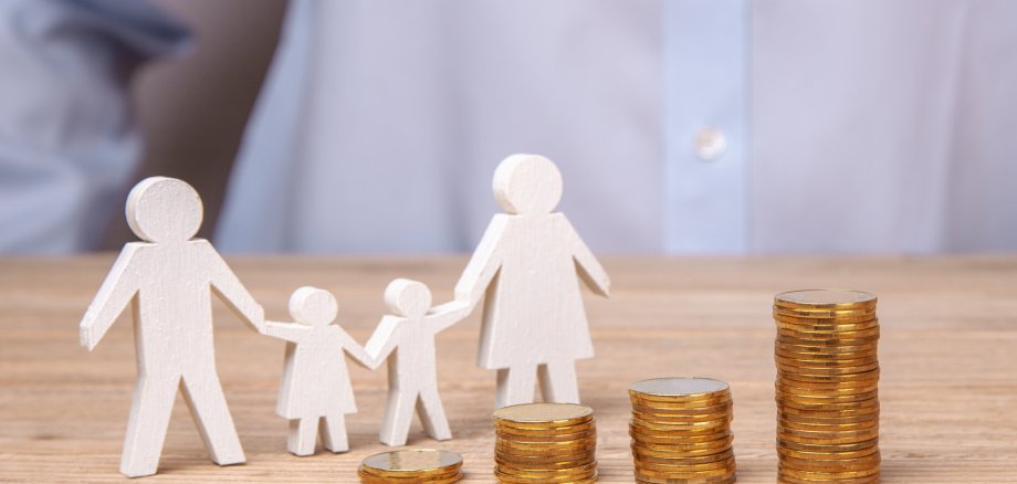 Holzfguren, die eine Familie darstellen stehen vor Münzgeld.