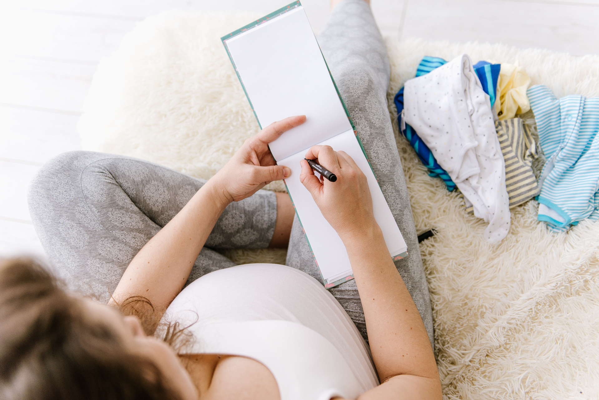Eine Schwangere Frau sitzt auf dem Bett und schreibt eine Liste.