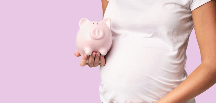 Eine schwangere Frau hält ein Sparschwein in der Hand.