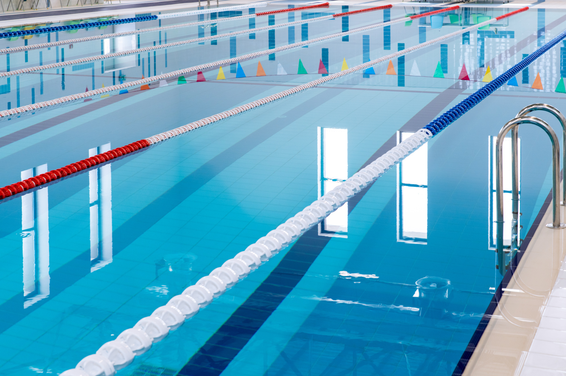 Schwimmbecken Blick auf ein blaues Hallenbad mit mehreren Bahnen, die durch rote, weiße und blaue Leinenbahnen voneinander getrennt sind.
