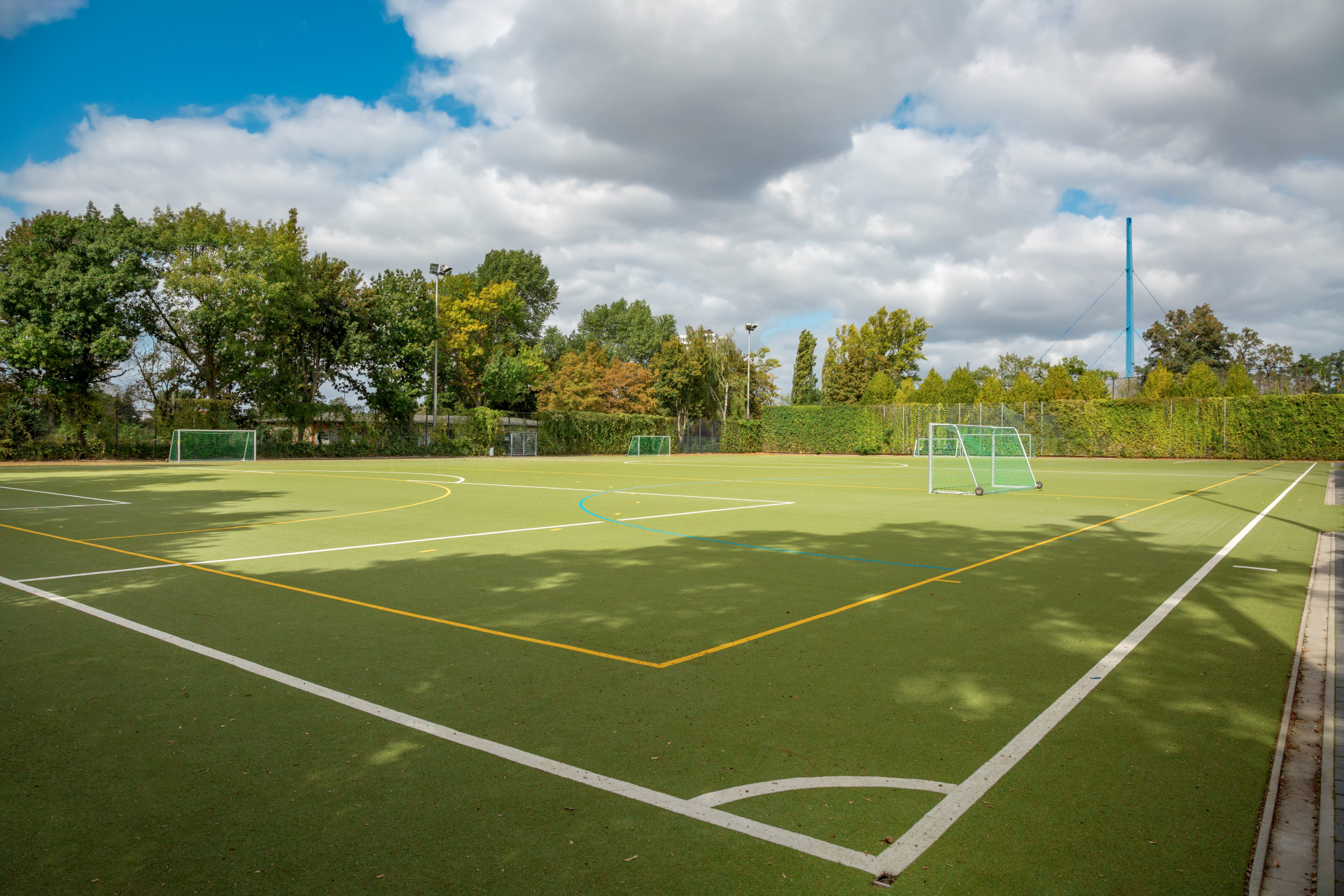 Sportplatz Ein grüner Kunstrasenplatz mit weißen und gelben Spielfeldmarkierungen und kleinen Fußballtoren.