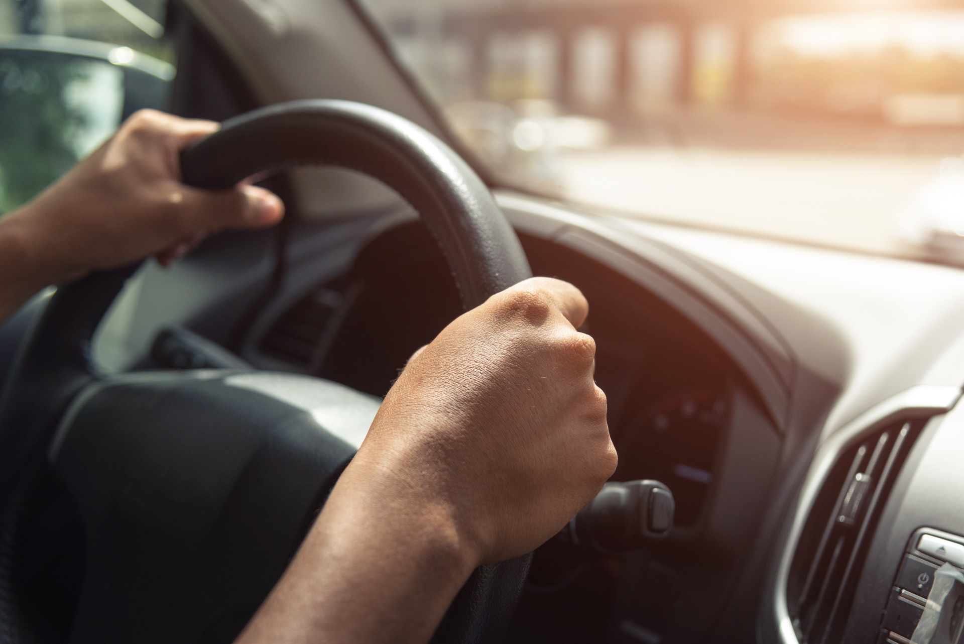 Eine Nahaufnahme von Händen, die ein Lenkrad in einem Auto greifen.
