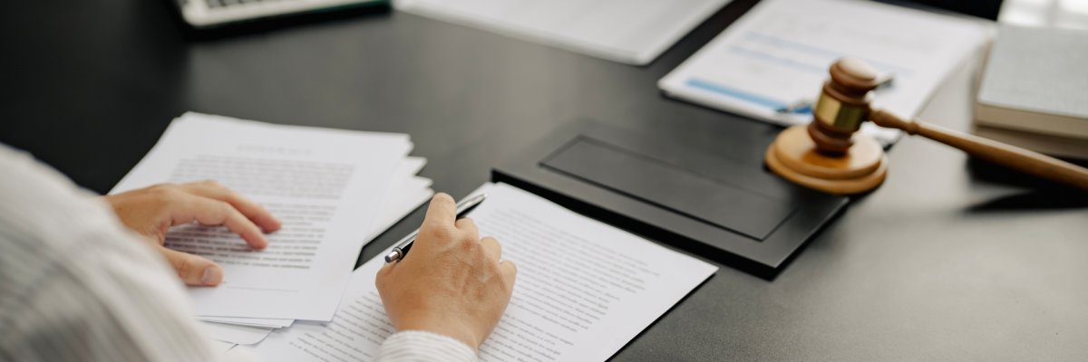 Eine Person bearbeitet Dokumente auf einem Schreibtisch. Rechts neben den Papieren liegt ein hölzerner Richterhammer.