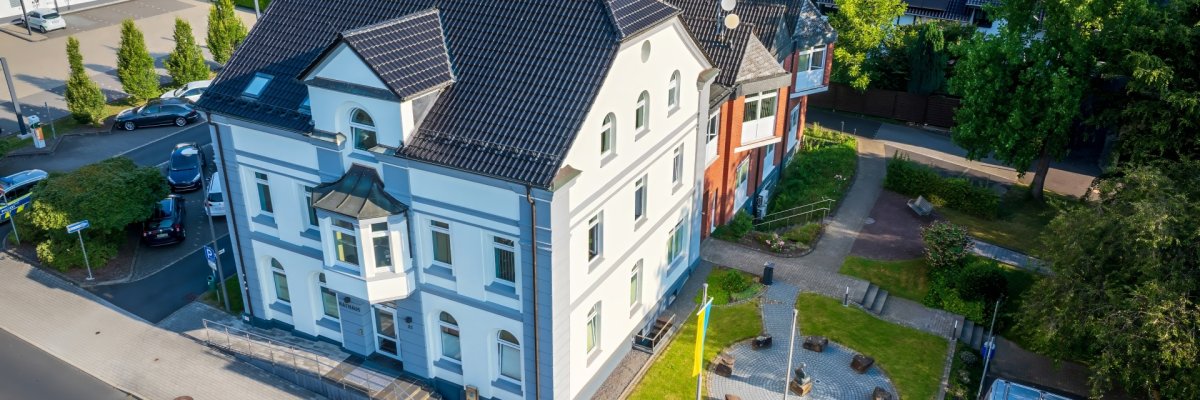 Luftaufnahme des Rathauses Overath Luftaufnahme des Rathauses Overath. Davor liegt eine Grünfläche mit einem kreisförmigen Steinweg. Im Vordergrund ist eine Straße und daneben eine Parkfläche mit Autos zu sehen.