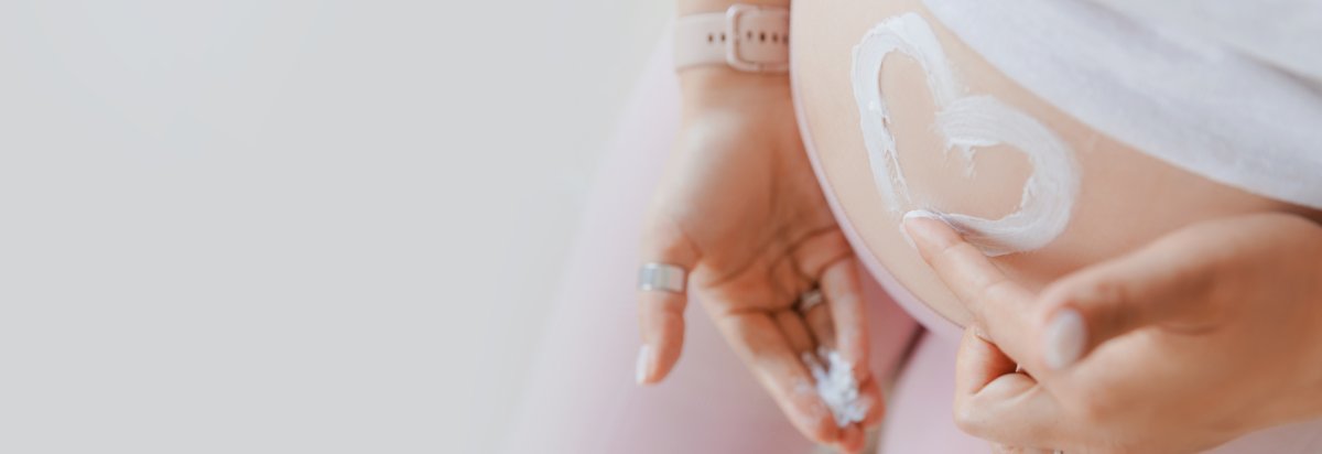 Schwangere Frau cremt ihren Babybauch ein. Herzform