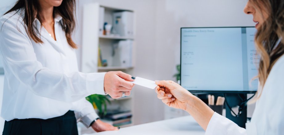 Eine Frau die ihre Patientenversicherungskarte an der Anmeldung abgibt