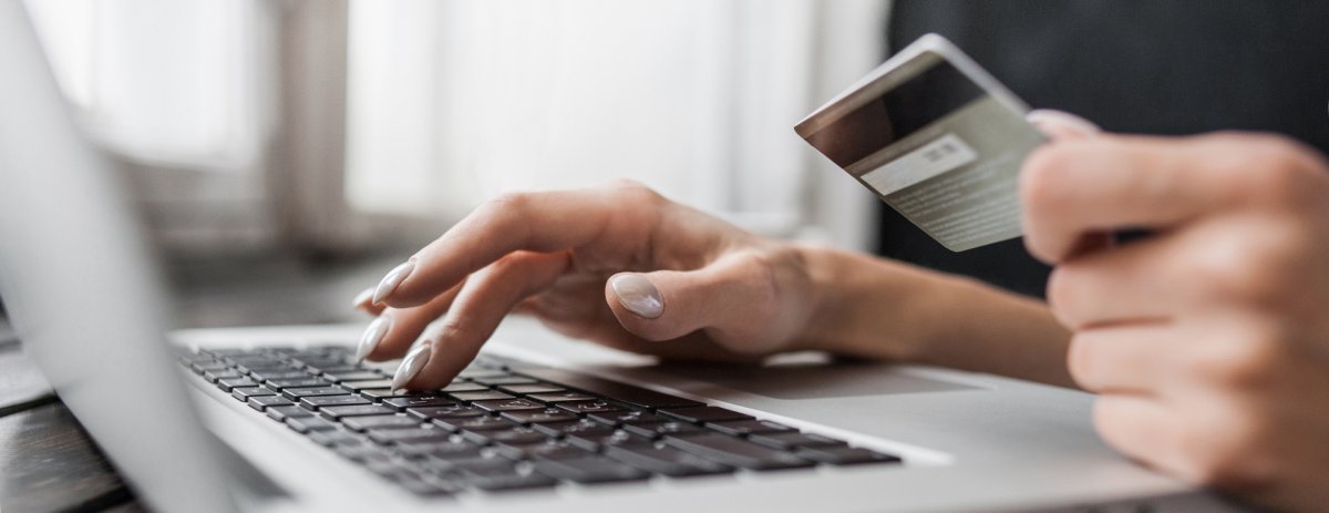 Frauenhand, welche eine Bankkarte hält, während die andere auf einem Laptop tippt.
