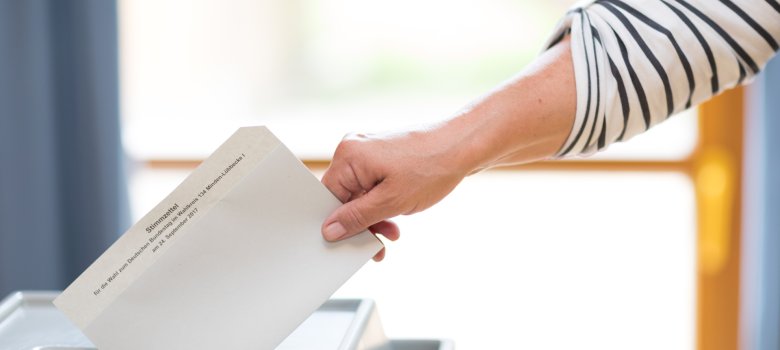 Stimmzettel wird in Wahlurne geworfen