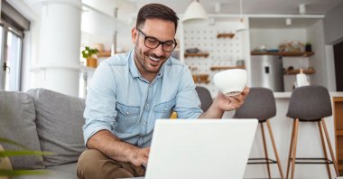 Young attractive man sitting on sofa at home working on laptop o