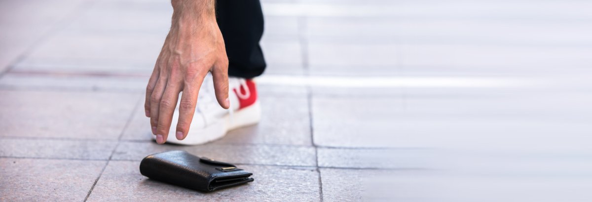 Männliche Hand beim Aufheben eines Portmonees vom Boden.