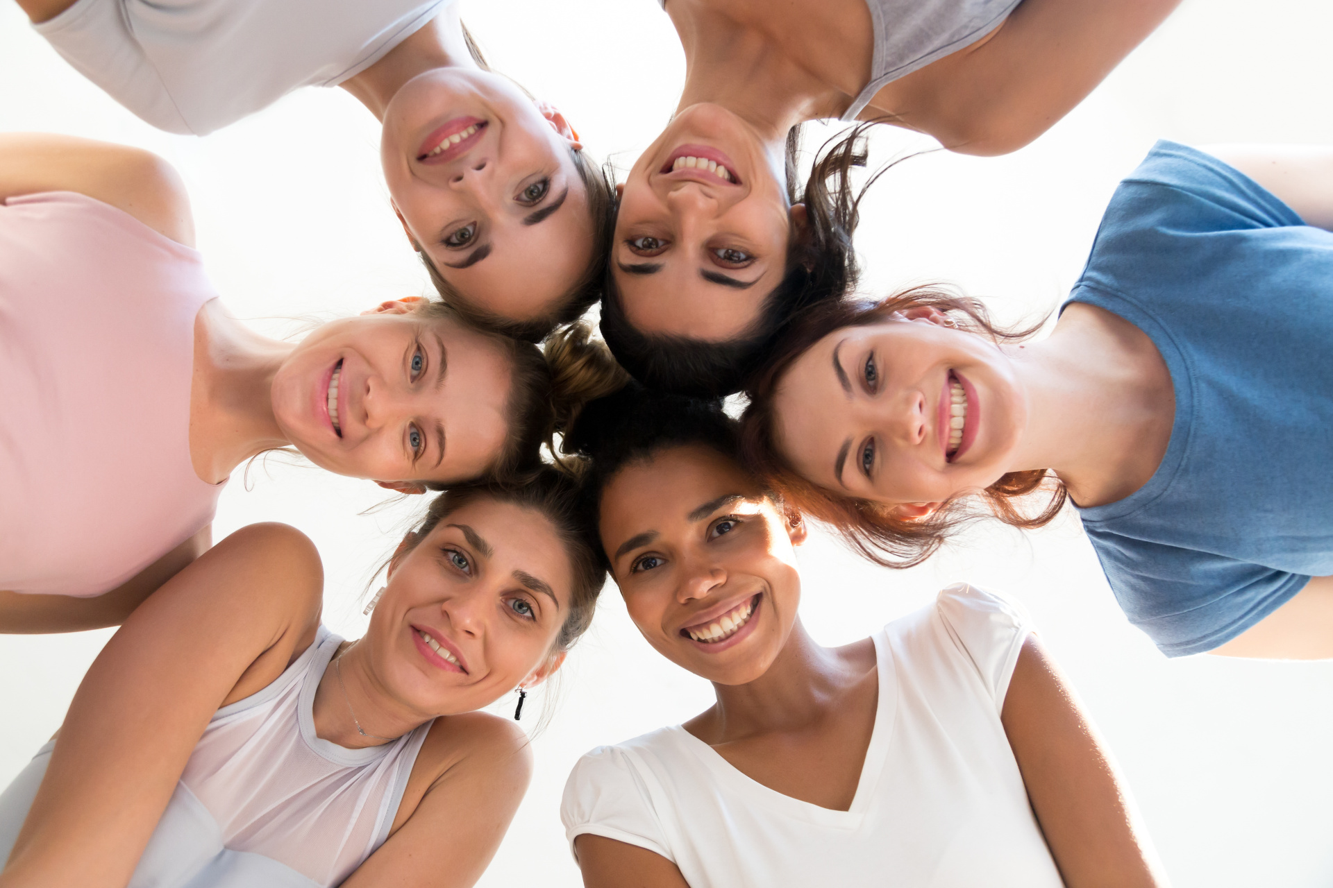Sechs unterschiedliche Frauen die ihre Köpfe mit dem Gesicht nach unten zu einem Kreis zusammengeführt haben