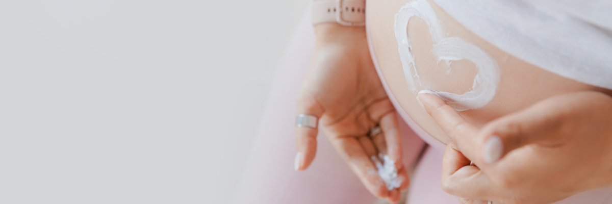 Eine schwangere Frau hat auf dem Bauch ein Herz aus Creme