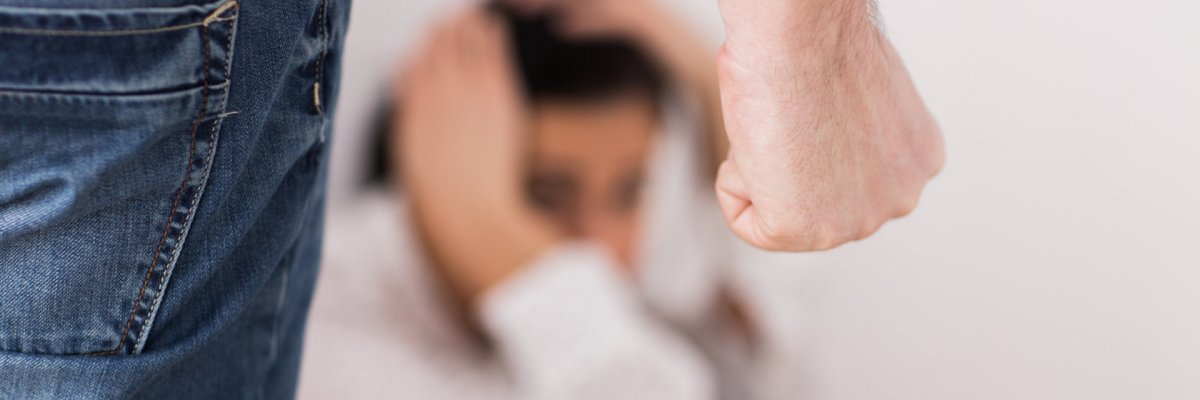 Eine Frau kauert aus Angst am Boden und ein Mann steht mit einer Faust vor ihr.