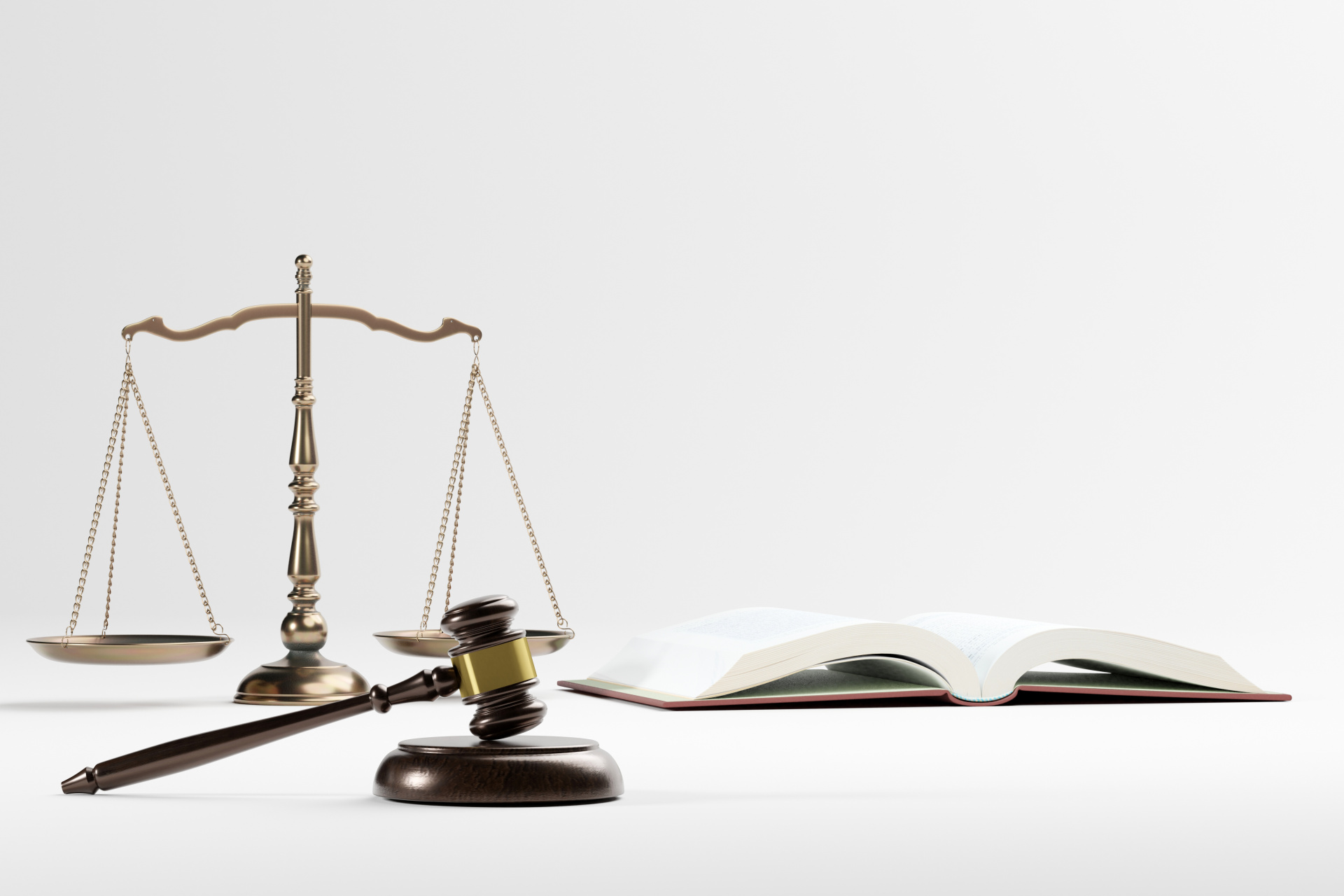 Eine goldfarbene Justizwaage, ein Richterhammer mit einem goldfarbenen Ring und ein aufgeschlagenes Buch liegen auf einem weißen Untergrund.